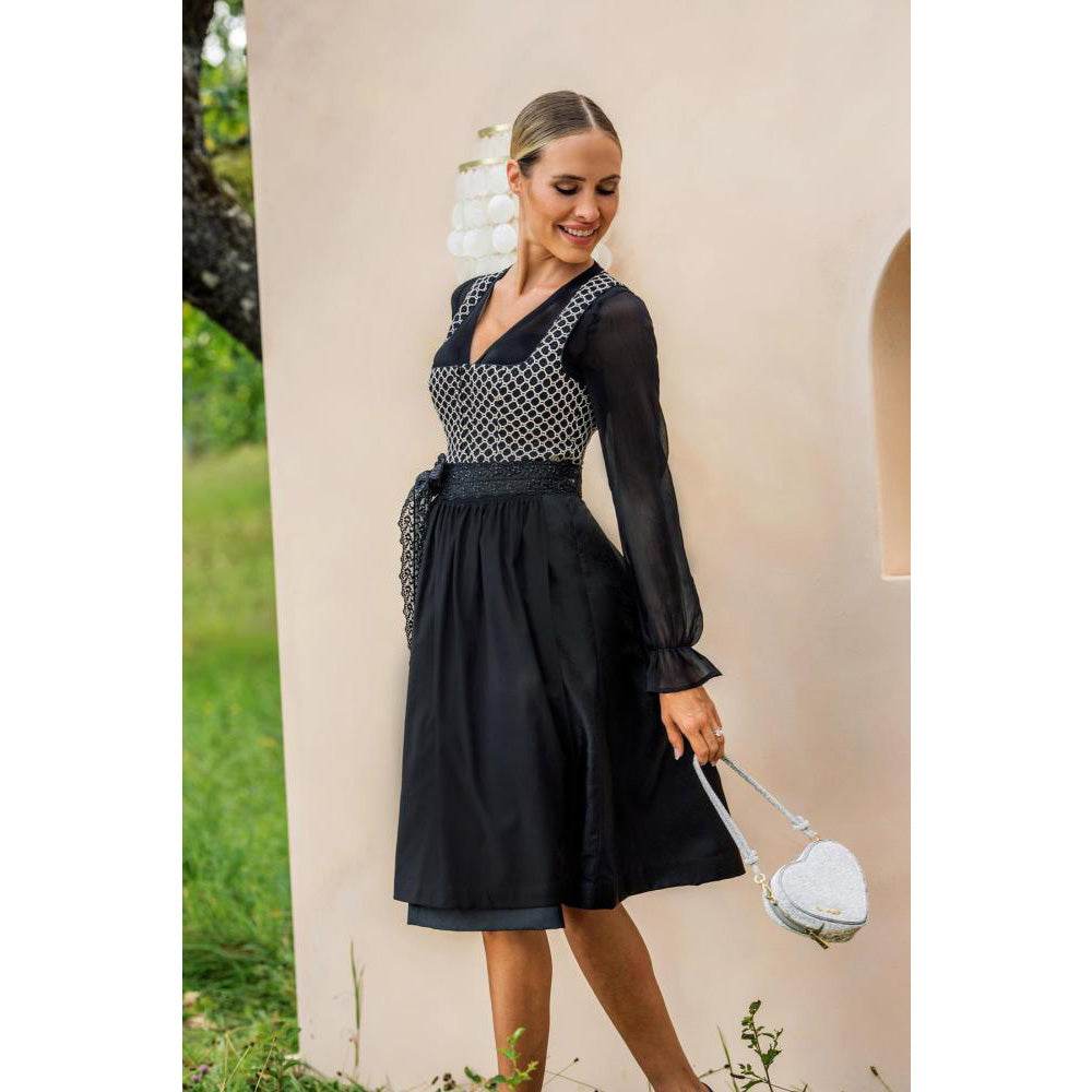 Zweiteiliges Dirndl in schwarz-creme mit Jacquard-Mieder im Rautenmuster, gepaspelten Ausschnitten und Reißverschluss vorne. Schwarzer Rock mit feinem Ornamentmuster, schwarze geraffte Schürze mit perlenverziertem Band und zwei verschließbaren Reißverschlusstaschen.