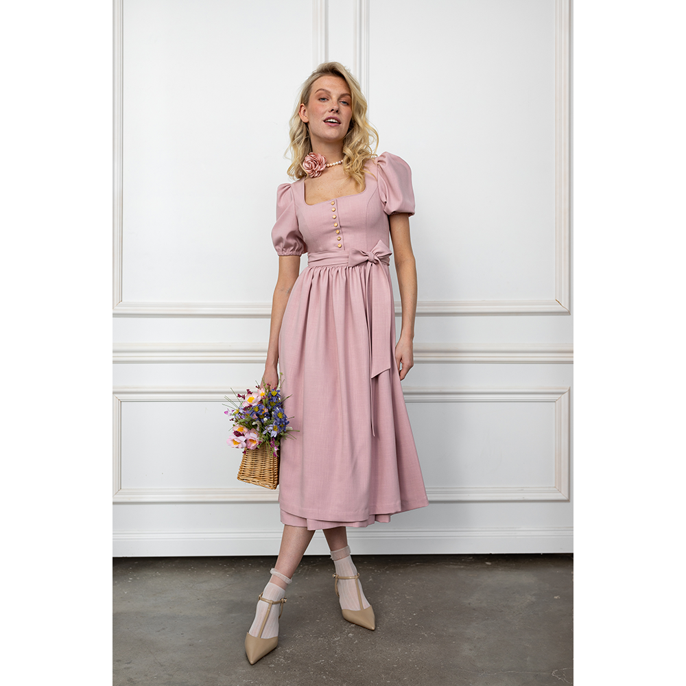 Verspieltes Dirndl in Flamingo-Rosa mit Puffärmeln, geradem Ausschnitt und Knopfleiste. Die passende Schürze ist mit einer Schleife gebunden, das Modell reicht bis knapp über das Knie.