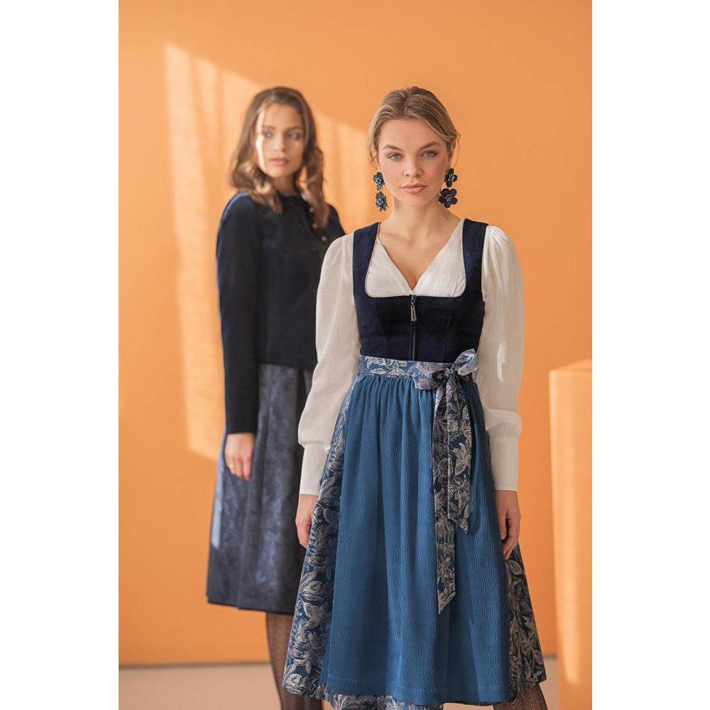 Weiße Dirndlbluse mit langen Puffärmeln aus leicht transparentem Stoff, V-Ausschnitt und Knopfleiste mit dekorativen Ösenknöpfen. Die breiten Manschetten sind mit je sechs Knöpfen in Perlenoptik verziert.