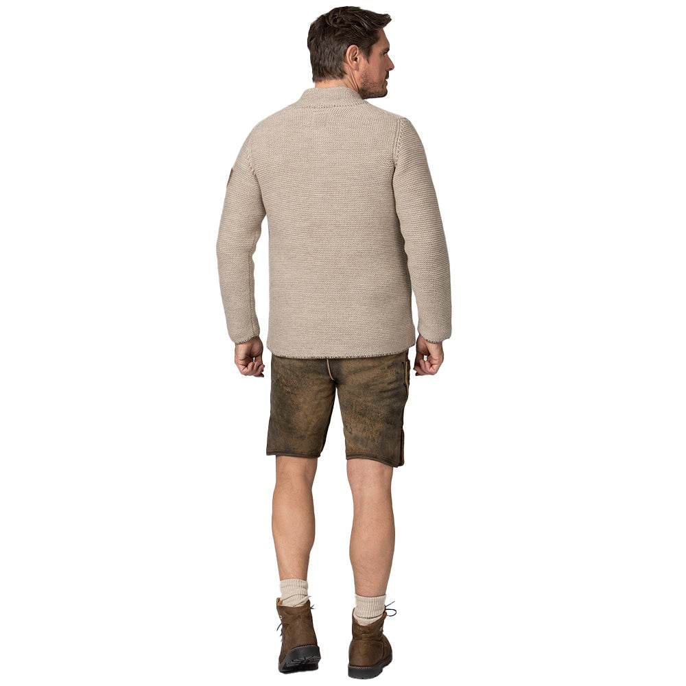 Strickjacke in hellem Sandton mit Stehkragen, aufgesetzten Taschen und rustikalen Hornknöpfen, im Sakko-Stil geschnitten, getragen als moderner Trachtenlook.