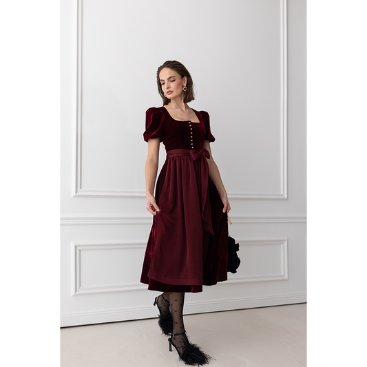Auffälliges rotes Samt-Dirndl mit modernem Mieder, geradem Ausschnitt und Knopfleiste. Die abnehmbare Schürze ist mit einer Schleife gebunden, das Dirndl endet knapp über dem Knie.