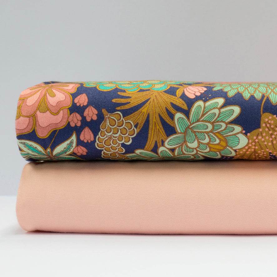 Stoffkombination mit einfarbigem apricotfarbenem Baumwollstoff für Oberteil und Rock sowie dunkelblauer Schürze mit buntem Blumenmuster.