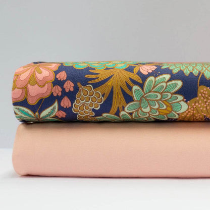 Stoffkombination mit einfarbigem apricotfarbenem Baumwollstoff für Oberteil und Rock sowie dunkelblauer Schürze mit buntem Blumenmuster.