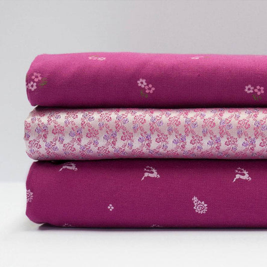 Stoffmuster für Dirndl mit Trachtenstoff in Fuchsia und Weiß mit kleinen Hirschen und Blumen für Erwachsene, kindliches Blümchenmuster in Pink und Grün sowie Schürze mit mehrfarbigem Blümchenjacquard in Weiß, Fuchsia, Blau und Lila.